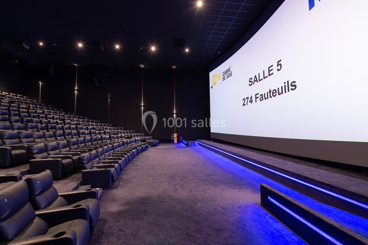 Salle de cinéma moderne avec écran large, rangées de fauteuils en cuir et éclairage tamisé.