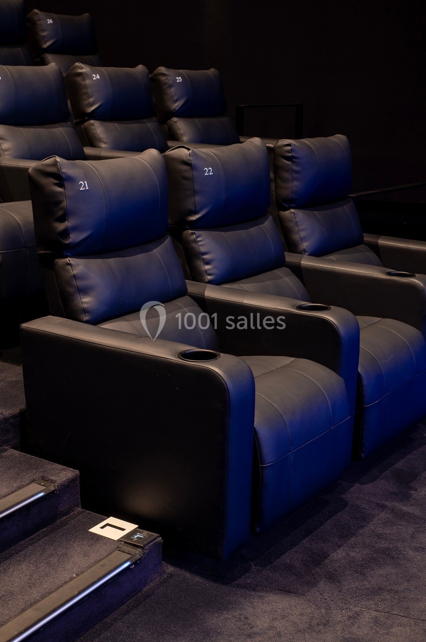 Fauteuils de cinéma en cuir noir numérotés, avec accoudoirs et porte-gobelets, disposés en gradins.