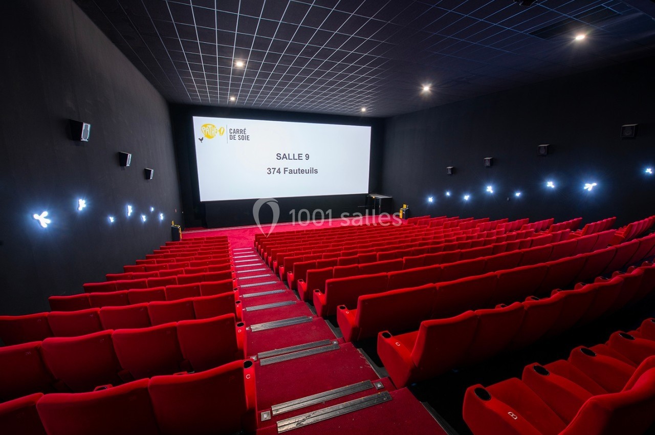 Salle de cinéma vide avec des rangées de fauteuils rouges, écran blanc affichant ’Salle 9 - 374 Fauteuils’.