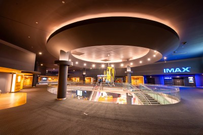 Vue intérieure d'un espace moderne avec escalier, escalator rouge et murs sombres décorés de motifs colorés.