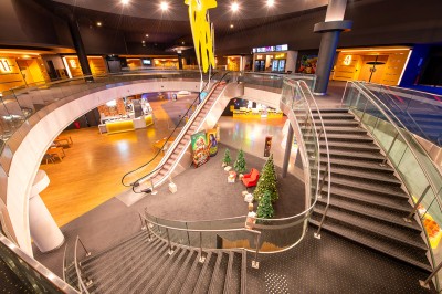 Vue intérieure d'un espace moderne avec escalier, escalator rouge et murs sombres décorés de motifs colorés.