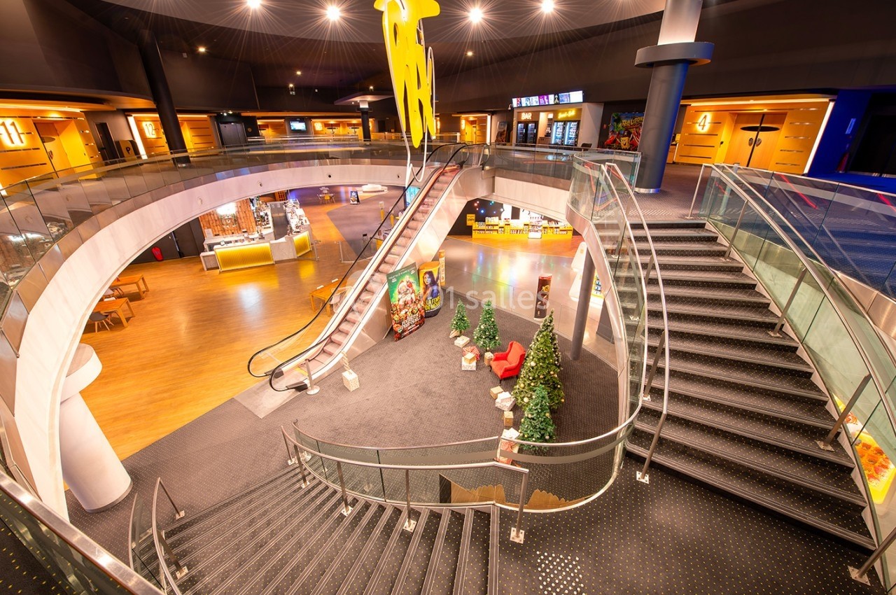 Vue intérieure d'un espace public avec escalier, escalator, décorations et zones d'accueil lumineuses.