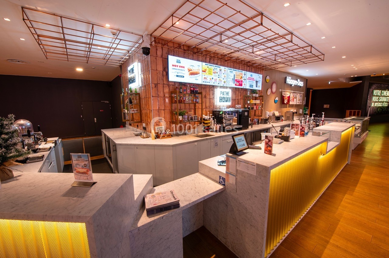 Comptoir moderne d'un cinéma avec menus affichés, machines à boissons et présentoirs de snacks.