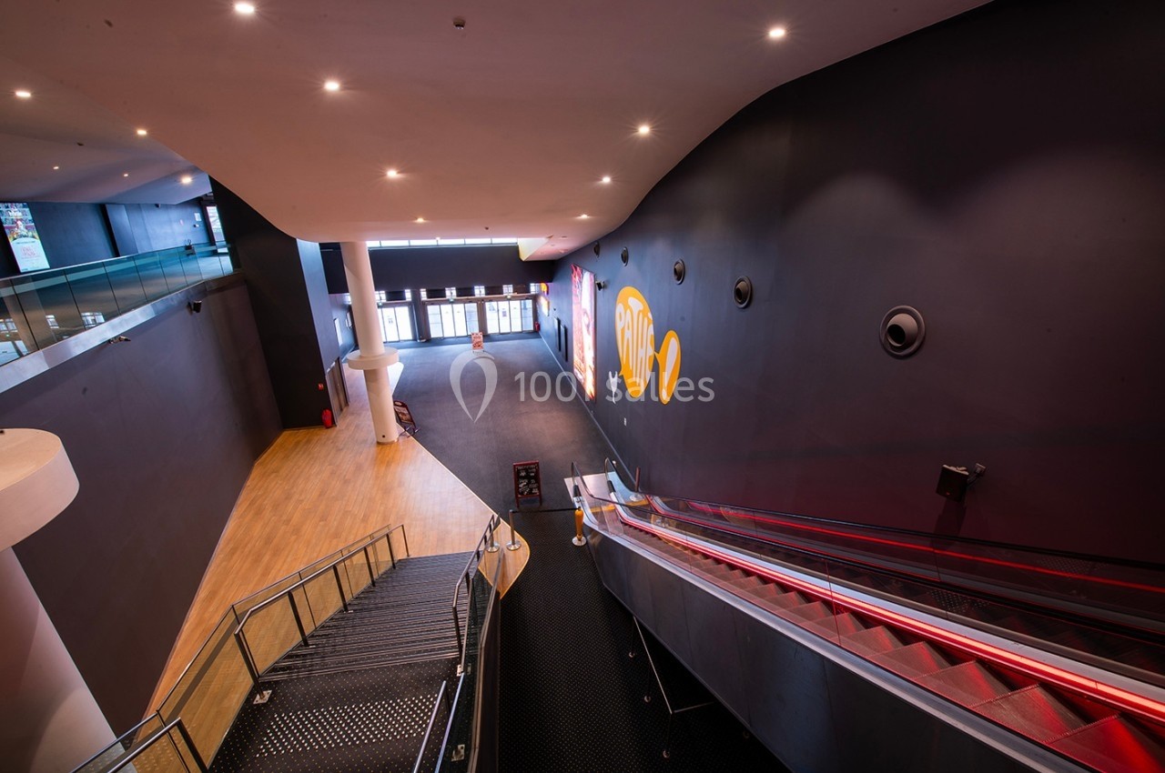 Vue intérieure d'un espace moderne avec escalier, escalator rouge et murs sombres décorés de motifs colorés.