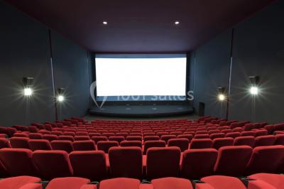 Salle de cinéma vide avec des rangées de sièges rouges et un éclairage tamisé.