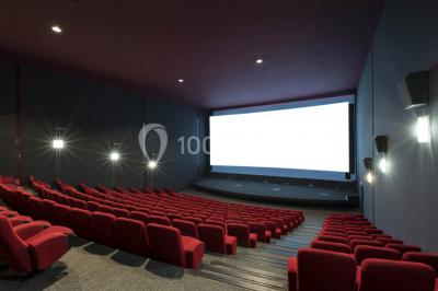 Salle de cinéma vide avec des rangées de sièges rouges et un éclairage tamisé.
