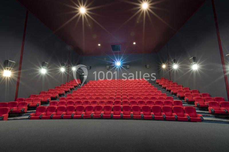 Salle de cinéma vide avec des rangées de fauteuils rouges et un écran éteint au fond.