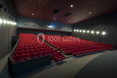 Salle de cinéma vide avec des rangées de sièges rouges et un éclairage tamisé.