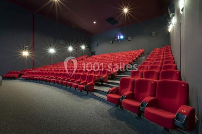 Salle de cinéma vide avec des rangées de sièges rouges et un éclairage tamisé.