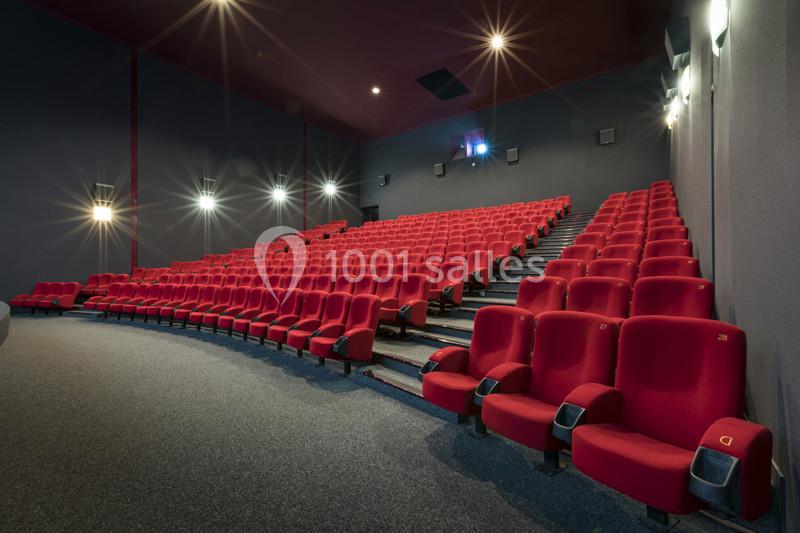 Salle de cinéma vide avec des rangées de fauteuils rouges et un éclairage tamisé.