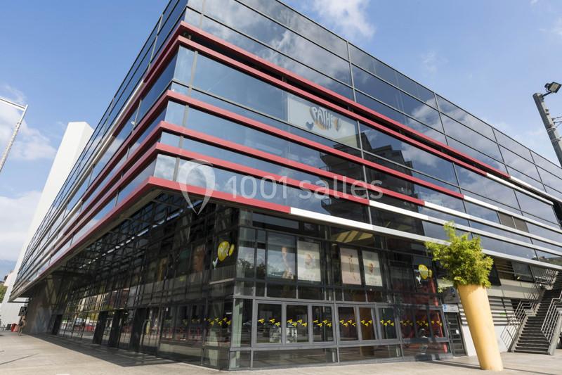 Façade moderne en verre et métal d'un bâtiment avec des lignes rouges et des reflets du ciel.