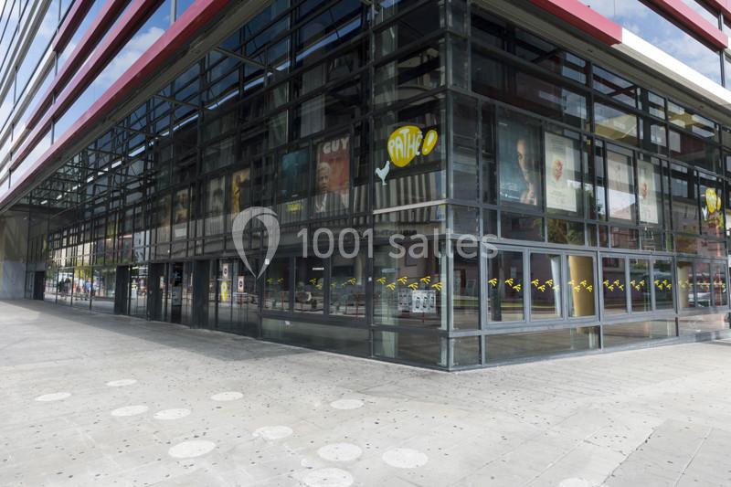 Façade vitrée d'un cinéma avec affiches de films visibles à l'intérieur, située sur une place pavée.