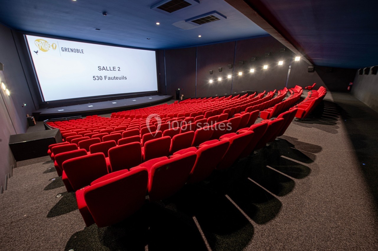 Salle de cinéma moderne avec 530 fauteuils rouges, écran large et éclairage tamisé.