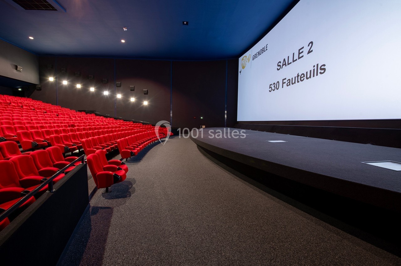 Salle de cinéma vide avec des rangées de fauteuils rouges et un grand écran affichant ’Salle 2, 530 fauteuils’.