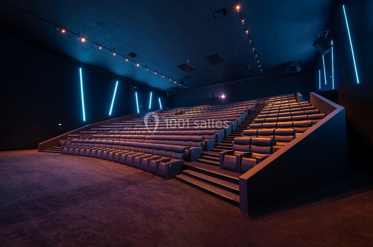 Salle de cinéma vide avec sièges inclinés en gradins, éclairage tamisé et lumières LED bleues sur les murs.
