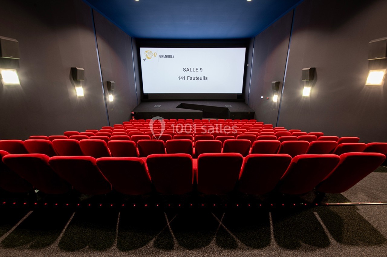 Salle de cinéma vide avec des rangées de fauteuils rouges et un écran affichant ’Salle 9, 141 fauteuils’.