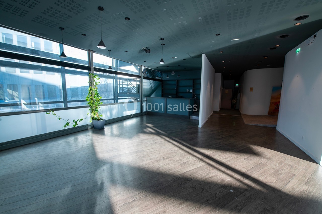 Salle lumineuse avec parquet, grandes fenêtres, plantes en pot et éclairage suspendu.