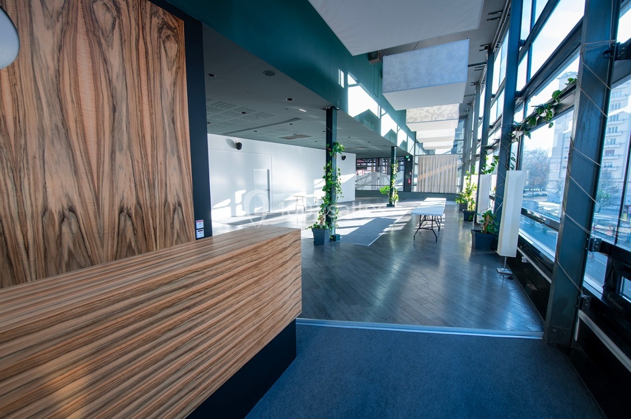 Espace intérieur lumineux avec un comptoir en bois, de grandes fenêtres et des plantes décoratives.