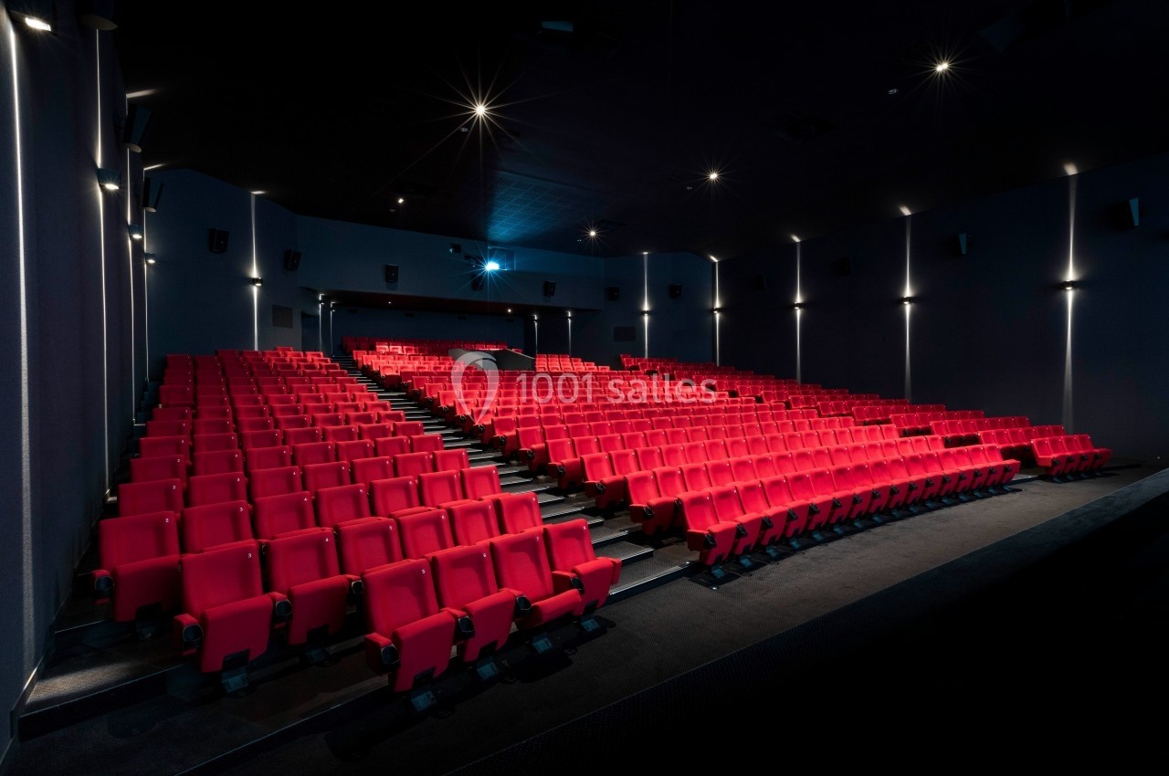 Salle de cinéma vide avec rangées de sièges rouges et éclairage tamisé.