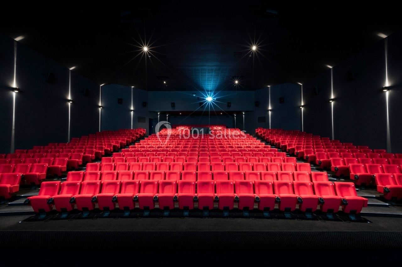 Salle de cinéma vide avec des rangées de sièges rouges et un projecteur allumé au fond.