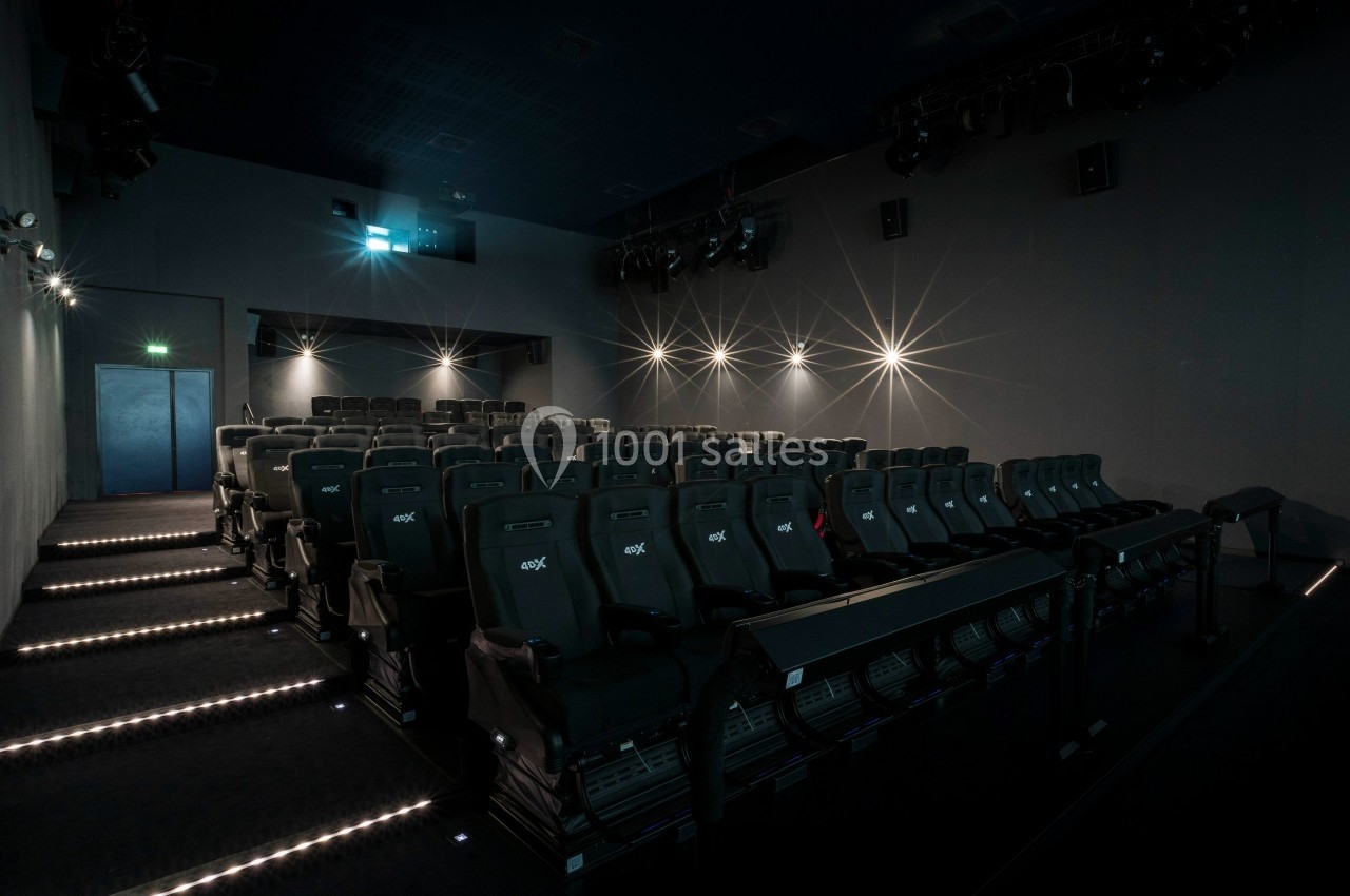 Salle de cinéma moderne avec rangées de sièges noirs, éclairage tamisé et allées lumineuses.