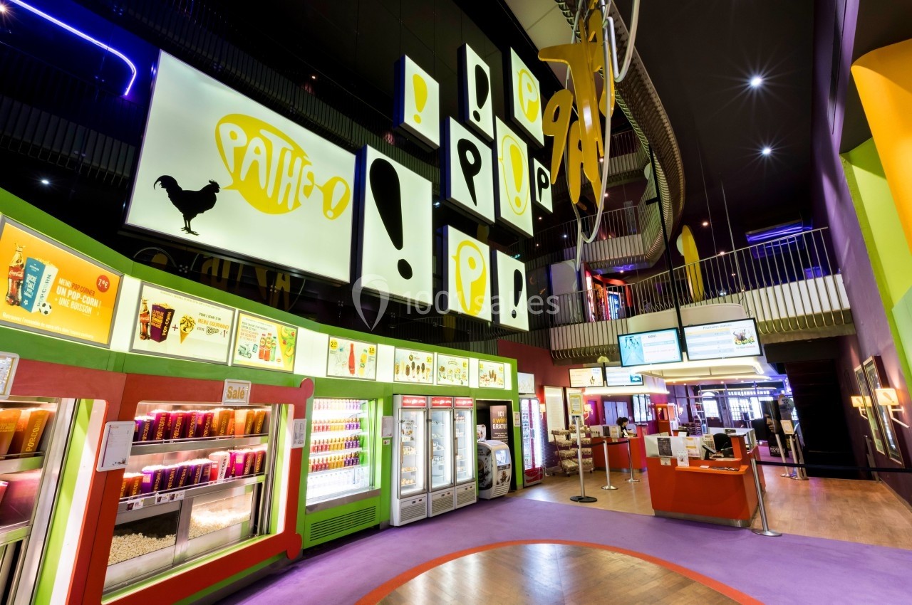 Hall d'entrée d'un cinéma avec comptoirs de vente, affiches lumineuses et décoration colorée.