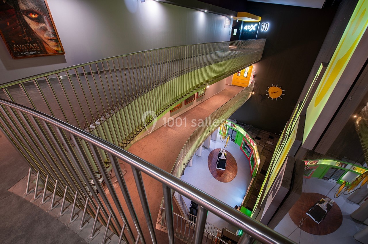 Vue intérieure d'un cinéma moderne avec des escaliers en colimaçon, affiches de films et éclairage tamisé.