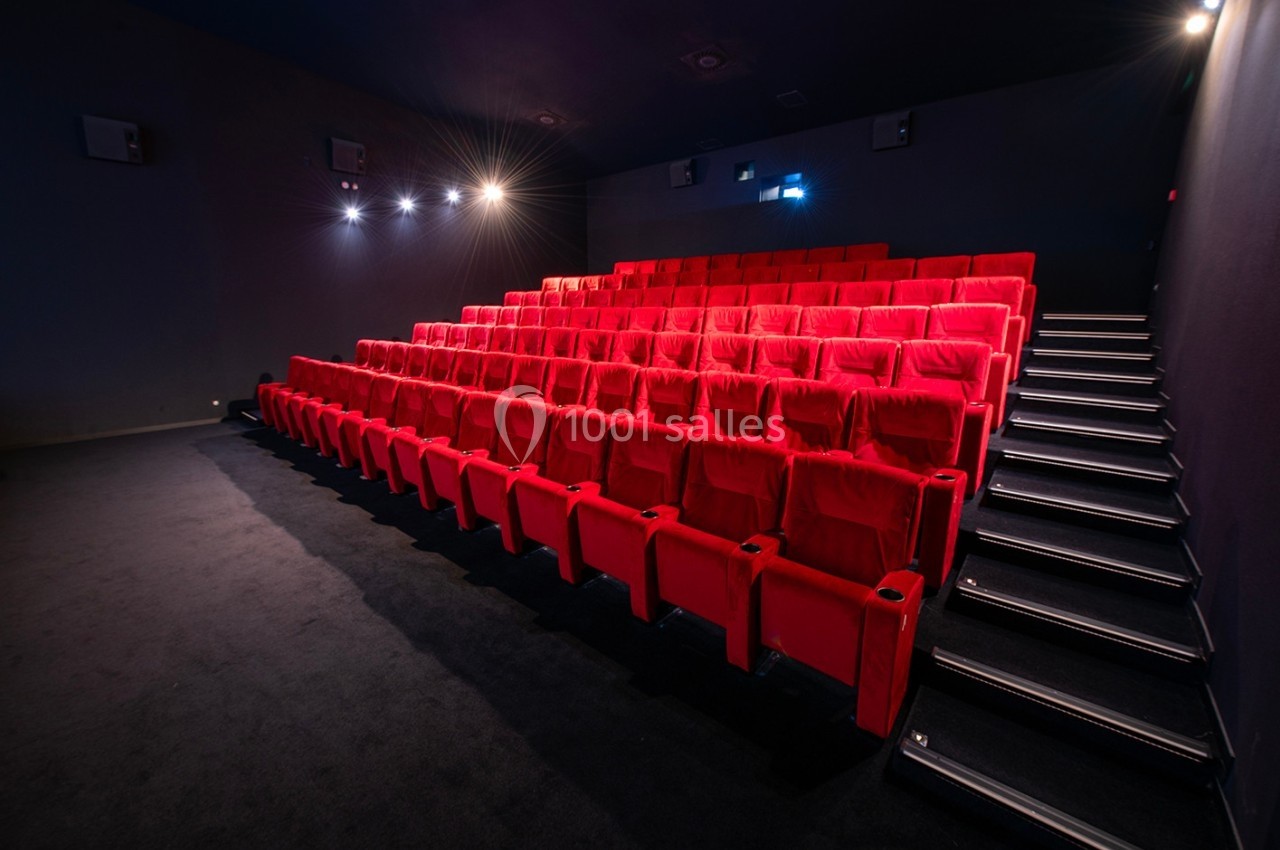 Salle de cinéma vide avec des rangées de fauteuils rouges et un éclairage tamisé.