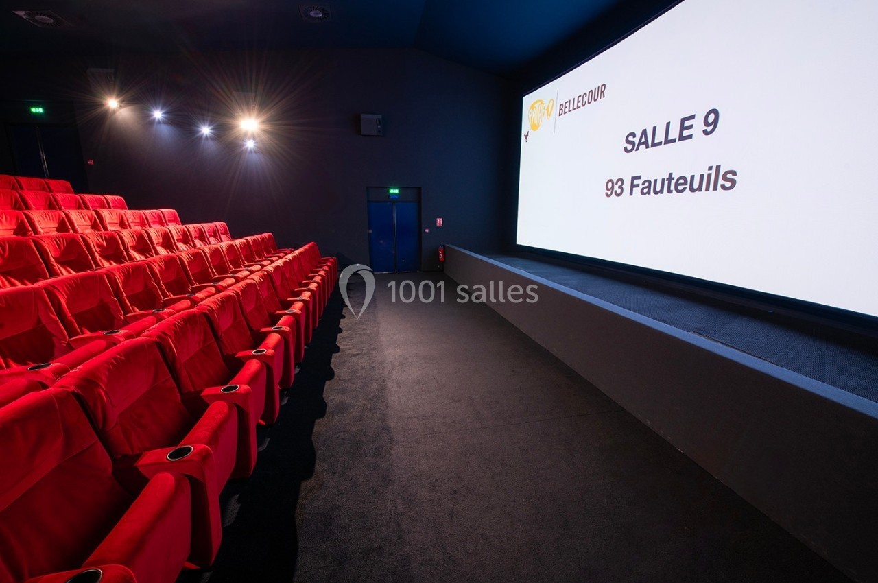 Salle de cinéma vide avec rangées de sièges rouges, écran blanc affichant ’Salle 9, 93 fauteuils’.