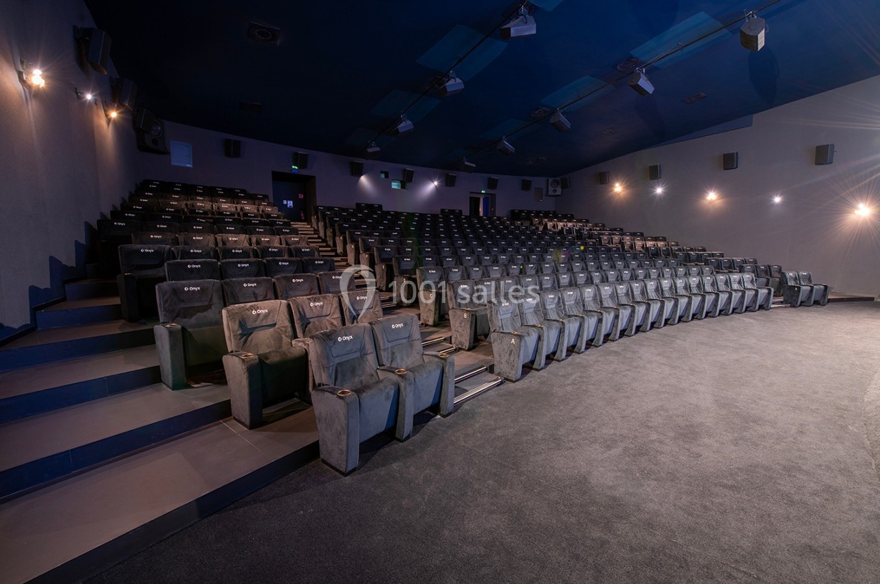 Salle de cinéma vide avec rangées de sièges noirs alignés et éclairage tamisé.