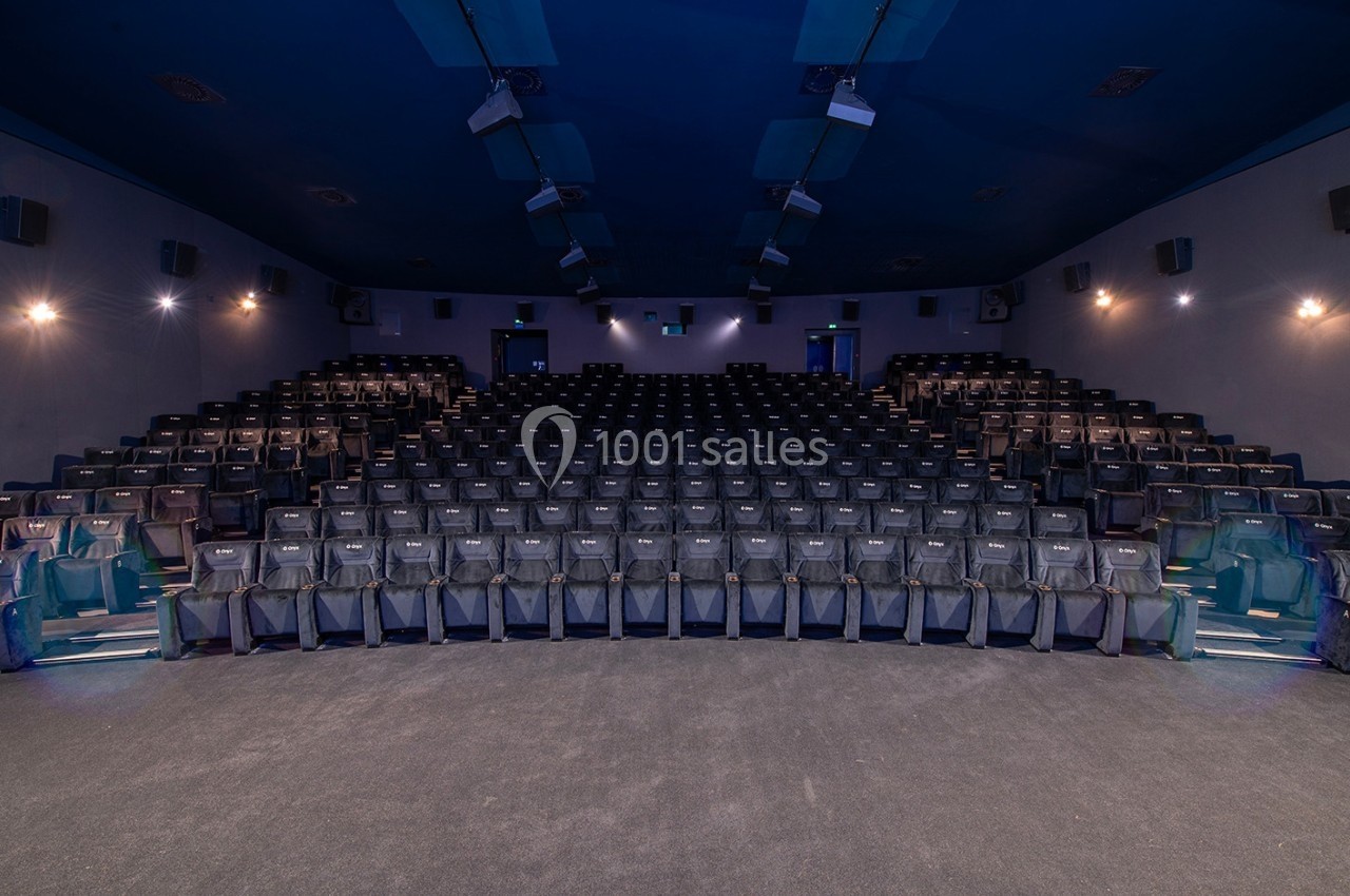 Salle de cinéma vide avec des rangées de sièges noirs alignés et un éclairage tamisé.