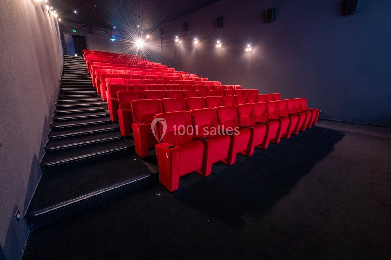 Salle de cinéma vide avec des rangées de fauteuils rouges et un éclairage tamisé.