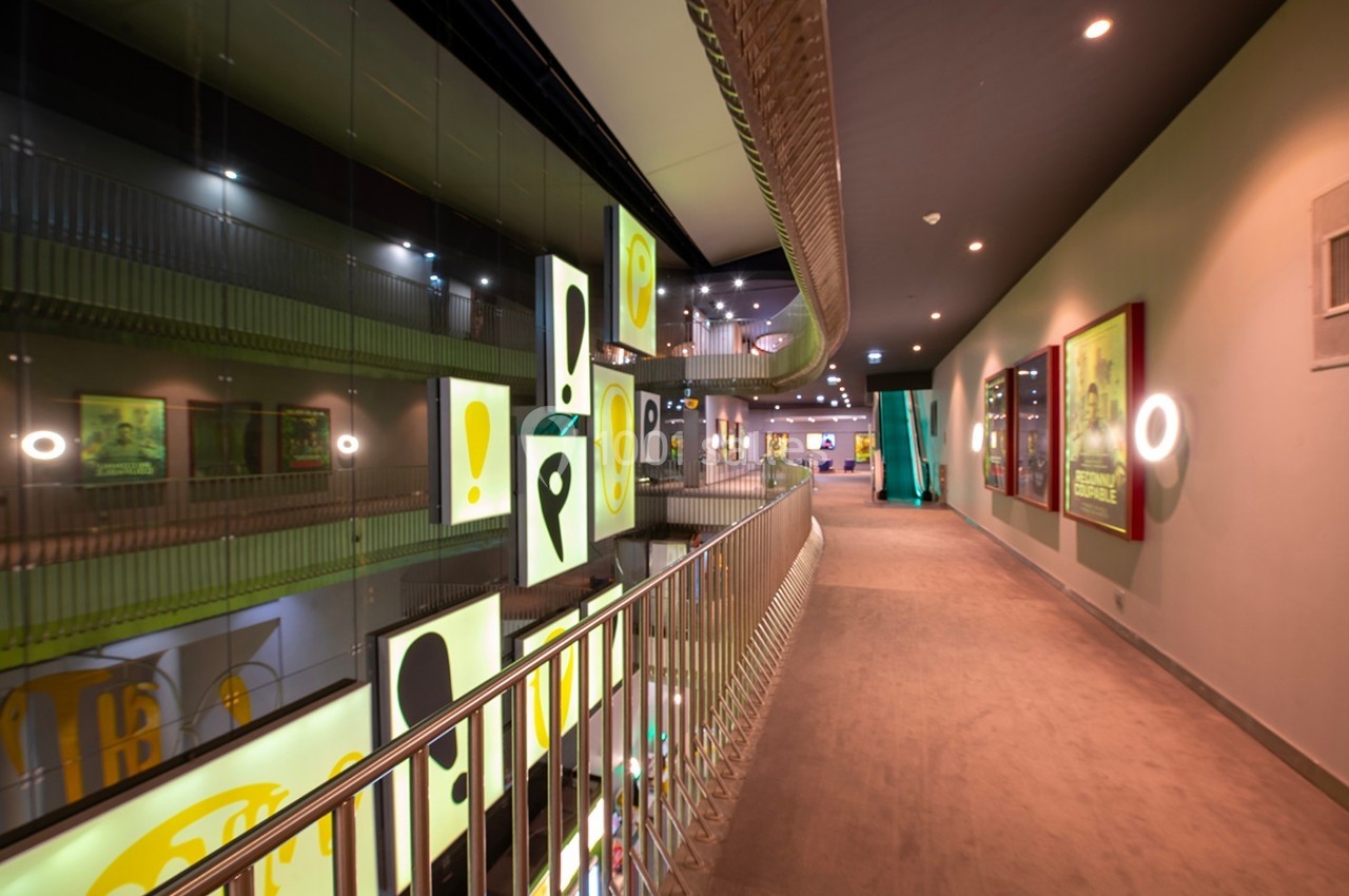 Couloir moderne avec balustrade métallique, affiches lumineuses suspendues et éclairage tamisé.