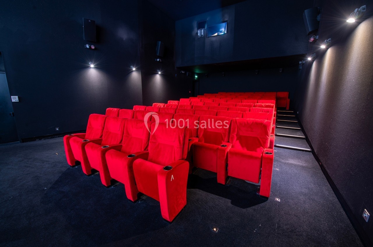 Salle de cinéma vide avec des rangées de fauteuils rouges alignés dans un espace sombre et éclairage tamisé.