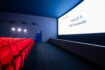 Salle de cinéma avec des rangées de fauteuils rouges et un écran affichant ’Salle 1, 318 fauteuils’.