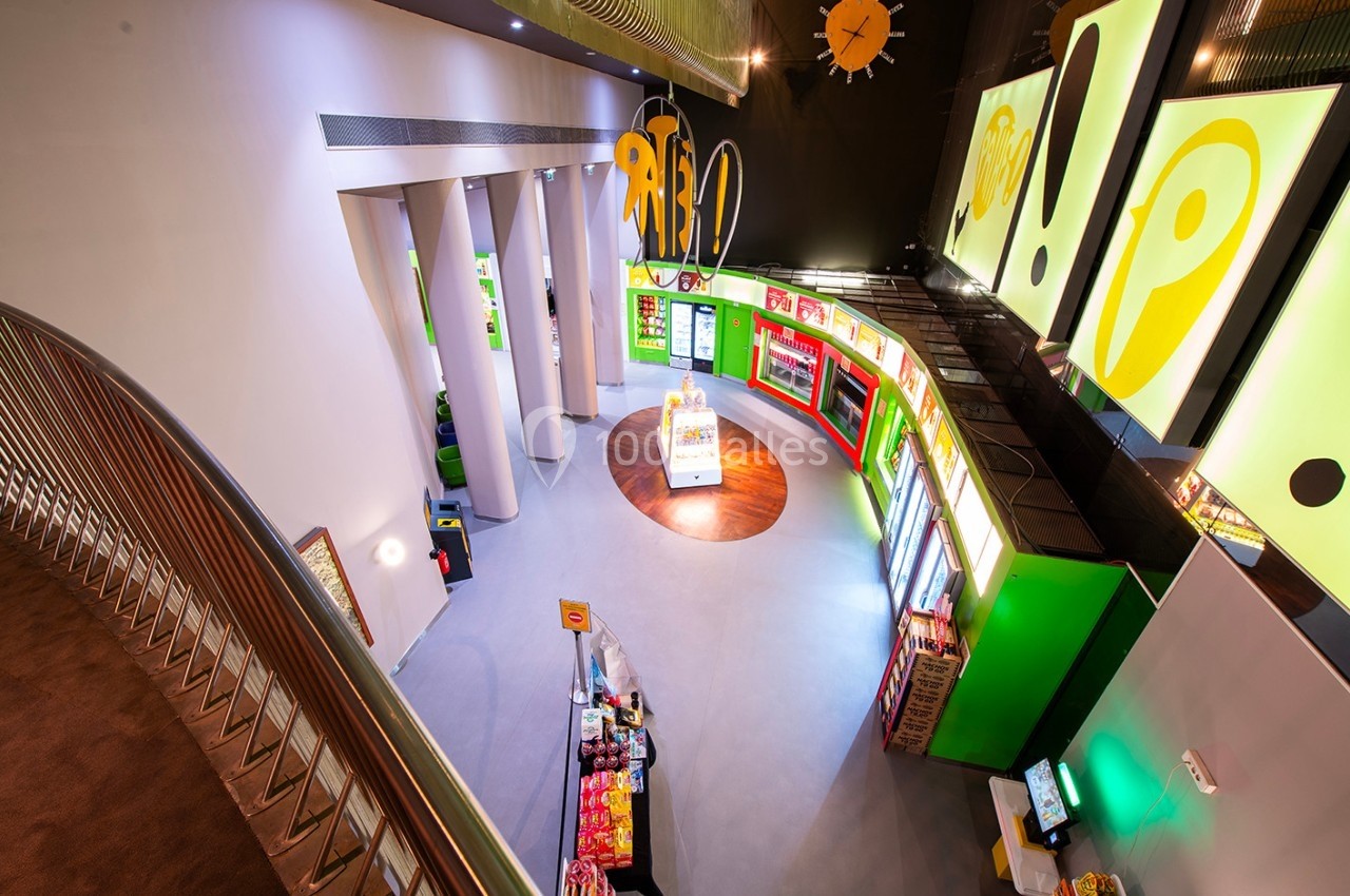 Vue plongeante sur un espace intérieur coloré avec des stands de snacks, des écrans lumineux et une architecture moderne.