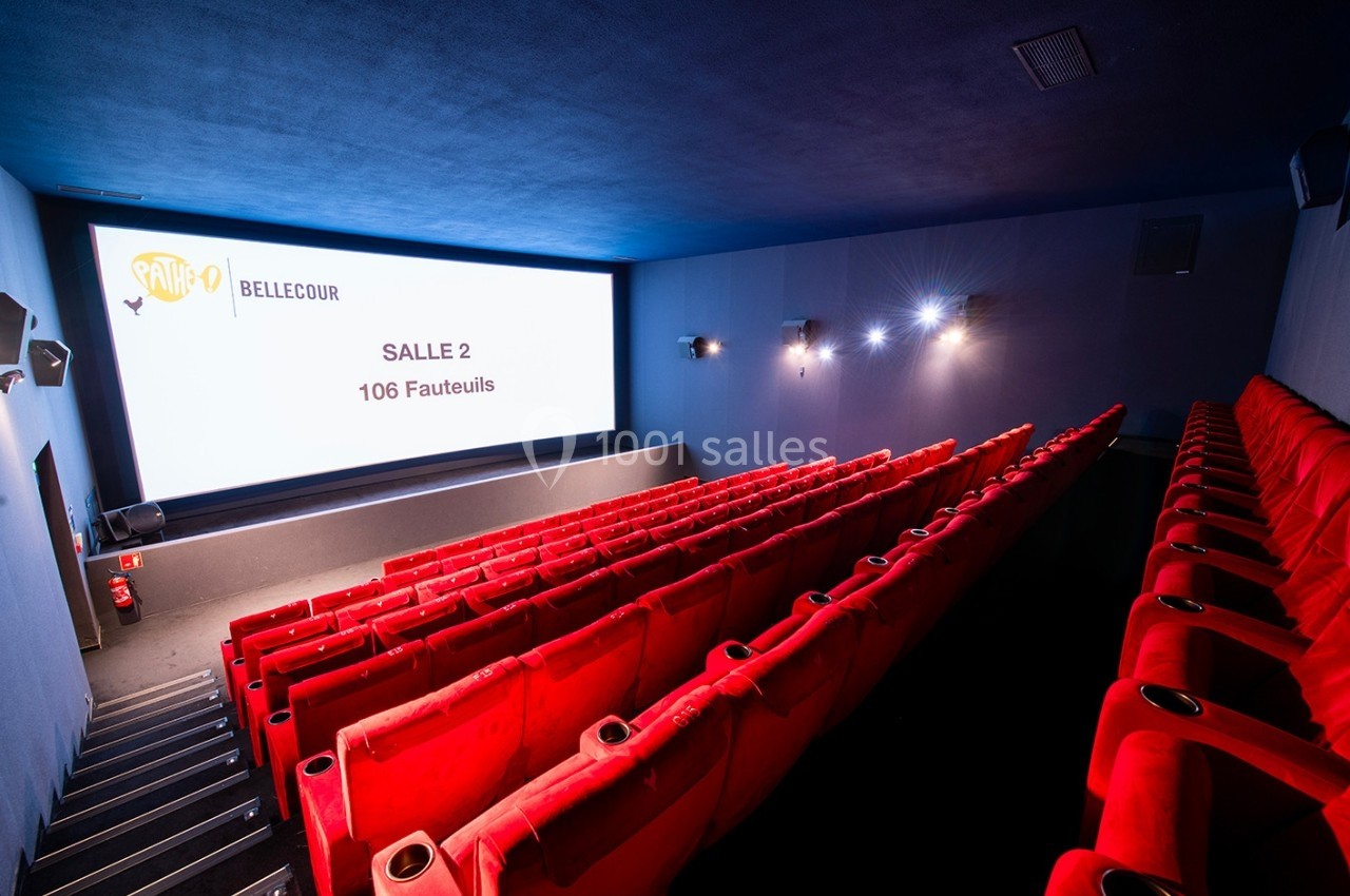 Salle de cinéma avec rangées de fauteuils rouges, écran blanc affichant ’Salle 2, 106 fauteuils’ et éclairage tamisé.
