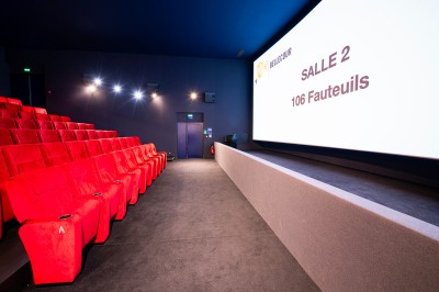 Salle de cinéma avec des rangées de fauteuils rouges et un écran affichant ’Salle 1, 318 fauteuils’.