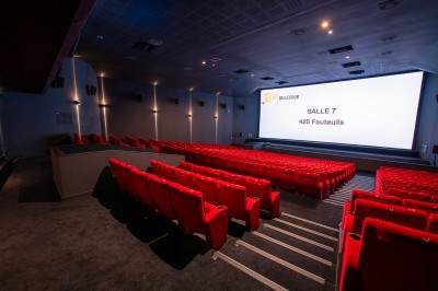 Salle de cinéma avec des rangées de fauteuils rouges et un écran affichant ’Salle 1, 318 fauteuils’.