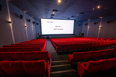 Salle de cinéma avec des rangées de fauteuils rouges et un écran affichant ’Salle 1, 318 fauteuils’.