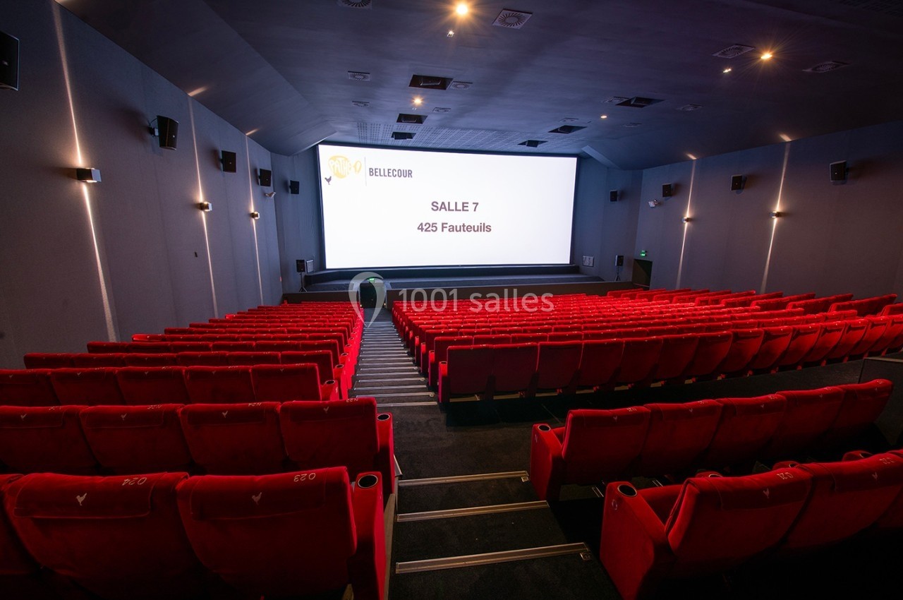 Salle de cinéma vide avec des rangées de fauteuils rouges et un grand écran affichant ’Salle 7, 425 fauteuils’.