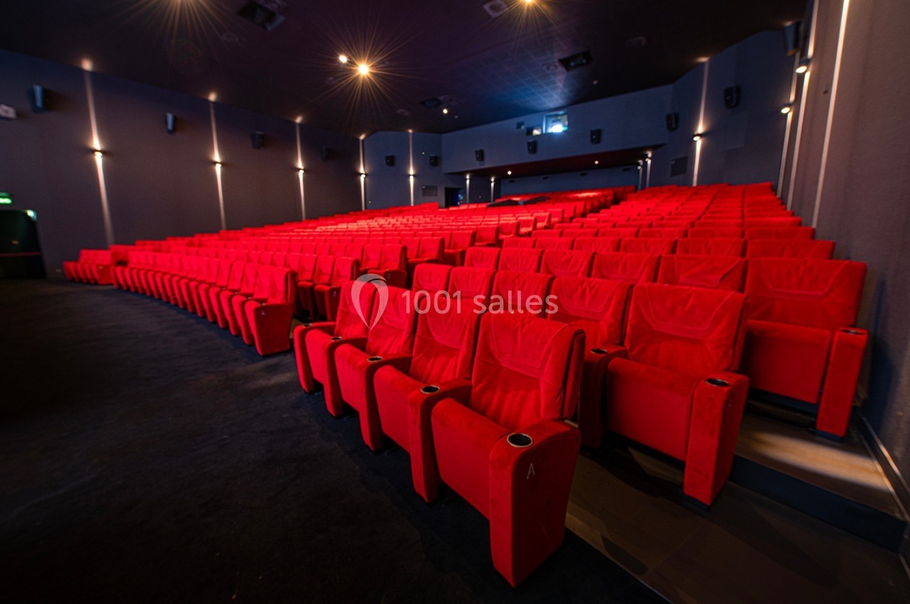 Salle de cinéma vide avec des rangées de fauteuils rouges et un éclairage tamisé.