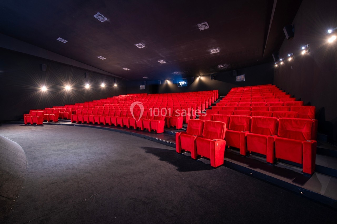 Salle de cinéma vide avec des rangées de fauteuils rouges et un éclairage tamisé.