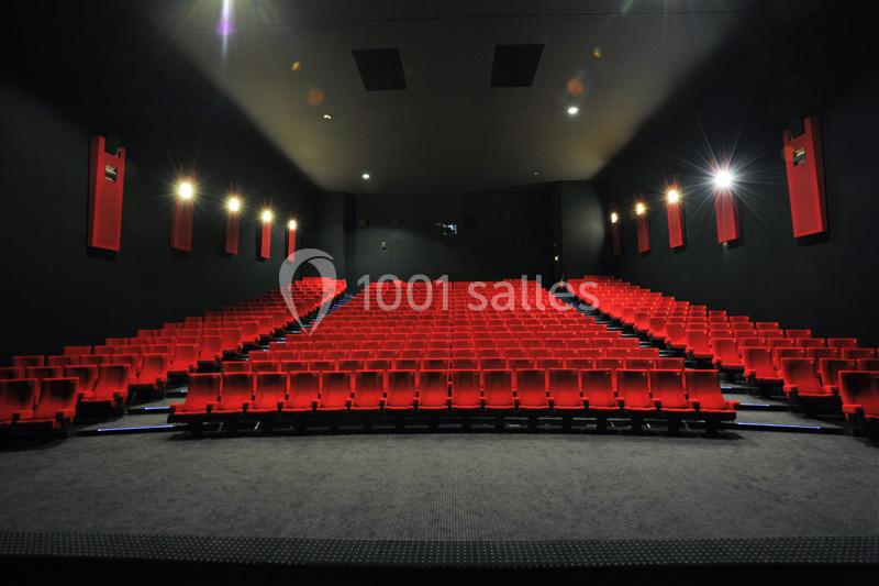 Salle de cinéma vide avec des rangées de fauteuils rouges et un éclairage tamisé.