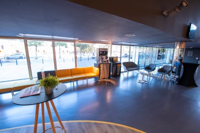 Couloir moderne avec éclairage tamisé, sièges incurvés, distributeurs automatiques et écrans muraux.