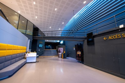 Couloir moderne avec éclairage tamisé, sièges incurvés, distributeurs automatiques et écrans muraux.