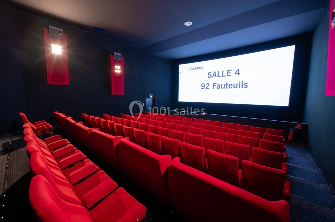 Salle de cinéma avec des rangées de fauteuils rouges vides, écran blanc affichant ’Salle 4, 92 fauteuils’.