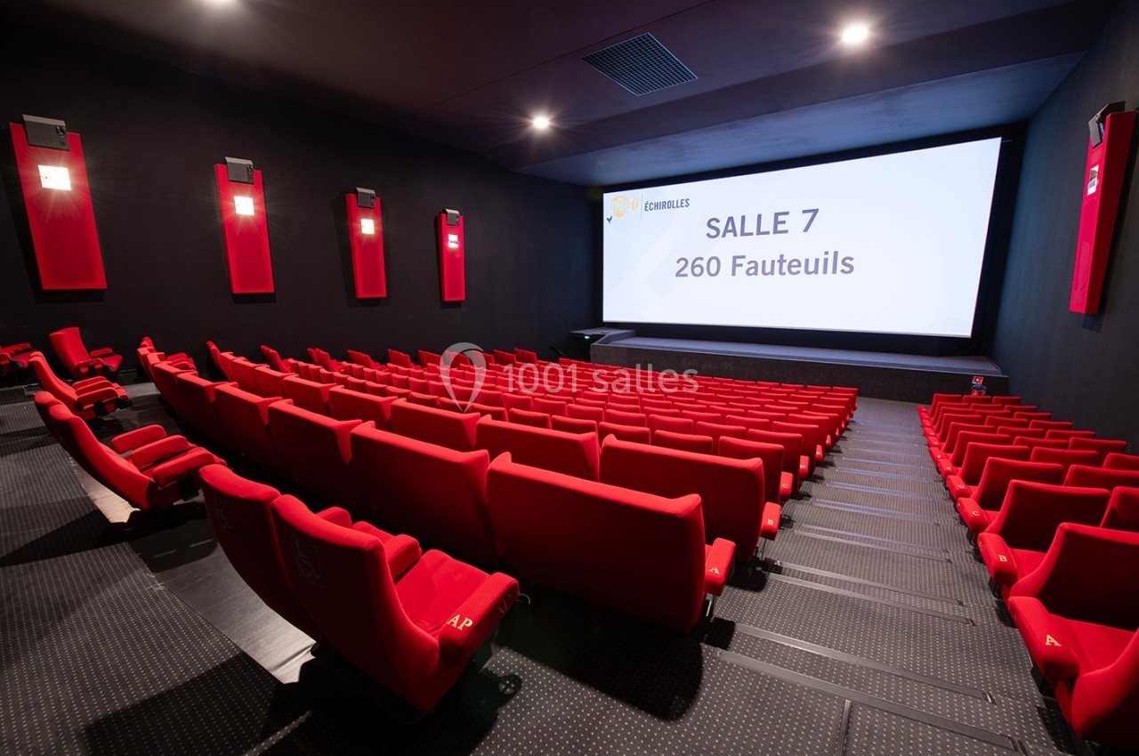Salle de cinéma moderne avec sièges rouges, écran affichant ’Salle 7, 260 fauteuils’ dans un espace sombre.