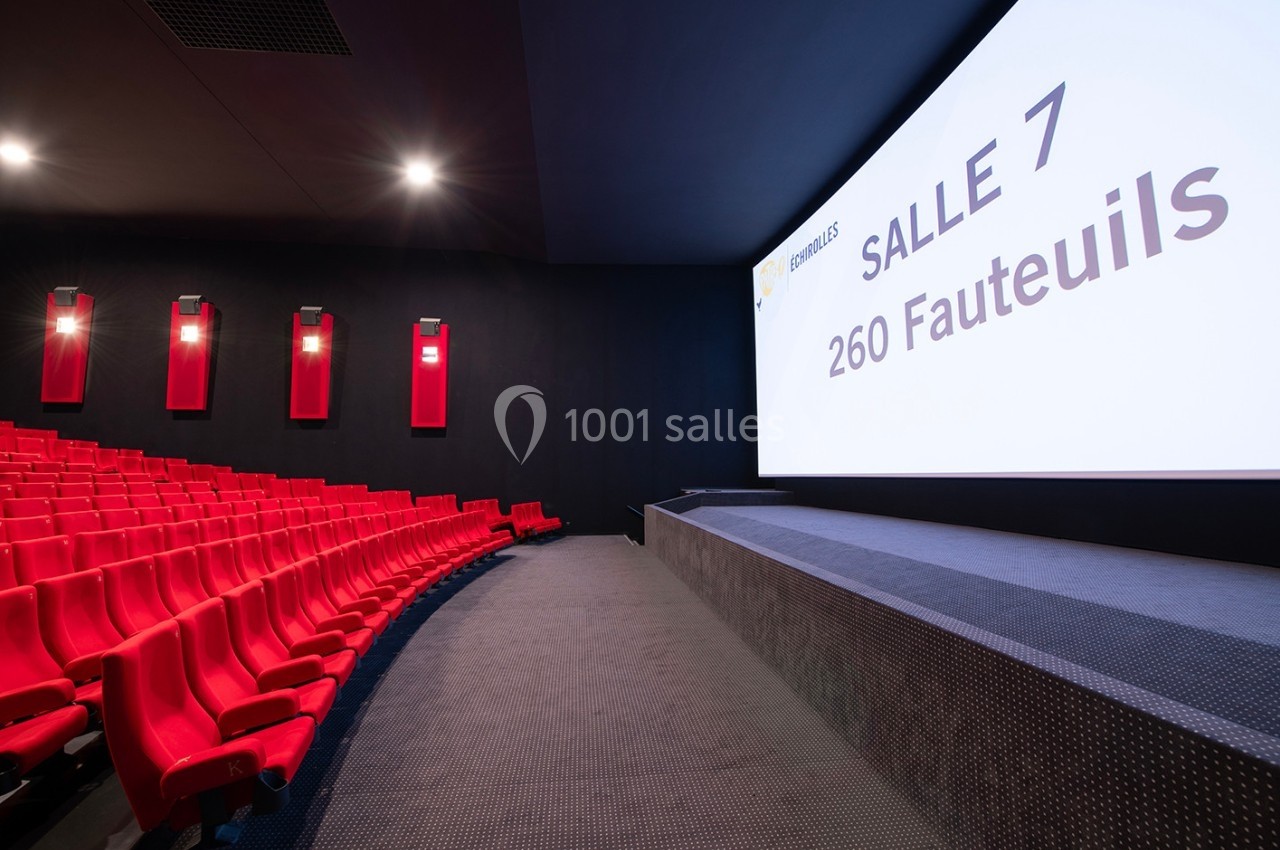 Salle de cinéma moderne avec rangées de sièges rouges et écran affichant ’Salle 7, 260 fauteuils’.