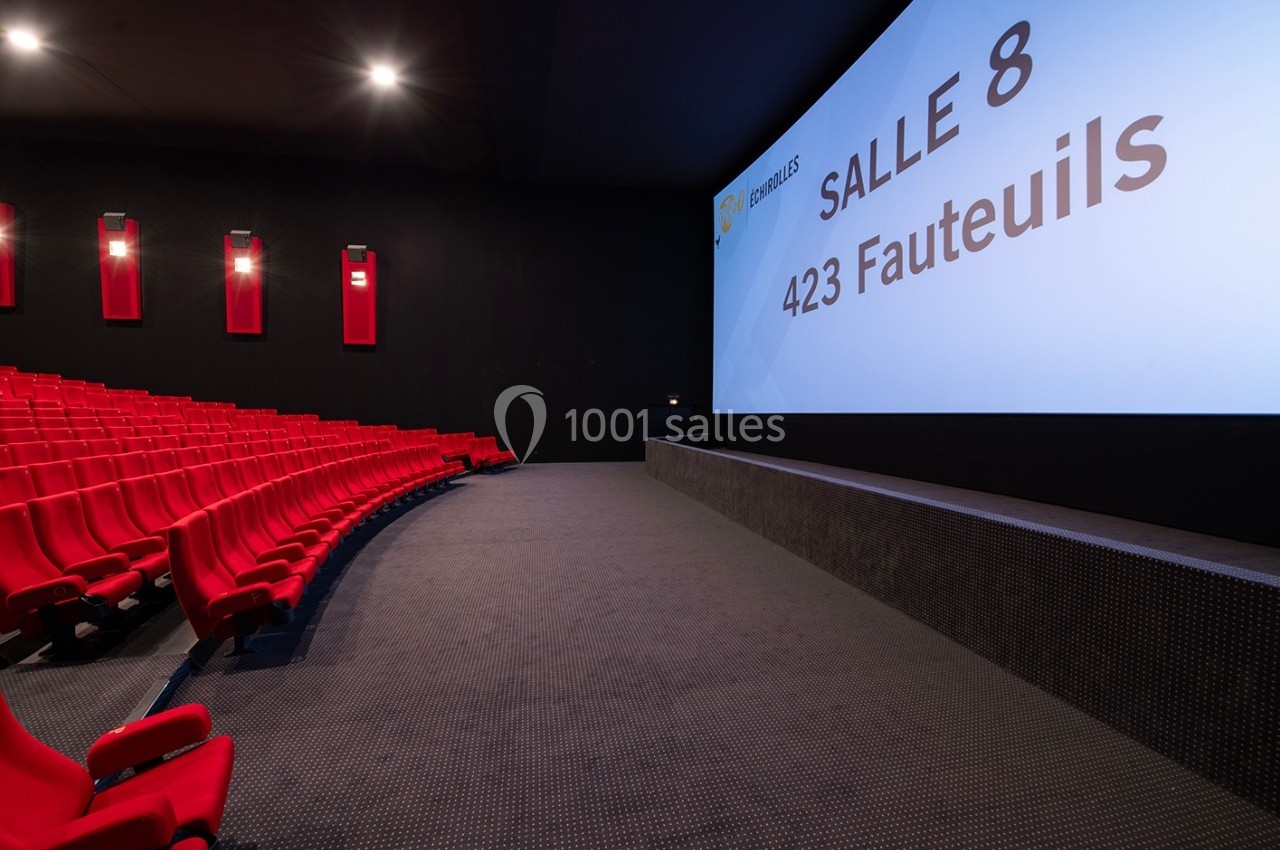 Salle de cinéma moderne avec des sièges rouges alignés et un écran affichant ’Salle 8, 423 fauteuils’.